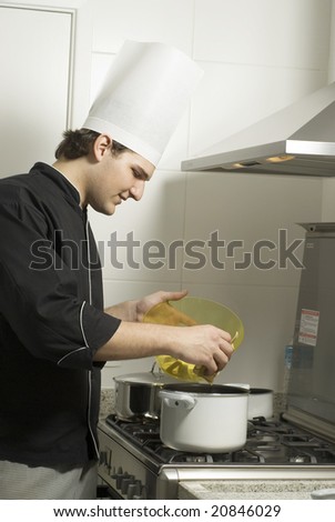 Young chef standing over a stove poring the contents from a bowl to a pot on the stove. Vertically framed photo.