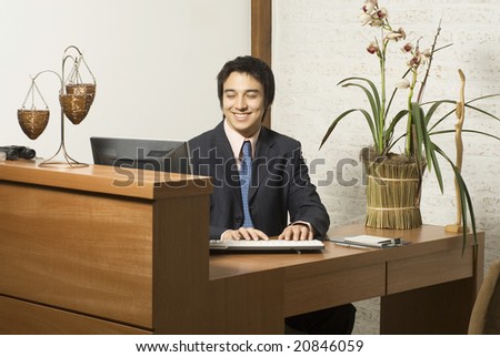 Businessman at desk smiling while typing at a computer. Horizontally framed photo.