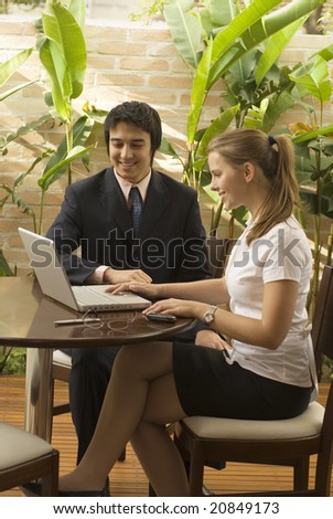 Smiling man and woman at a desk looking at a laptop computer. Vertically framed photo.