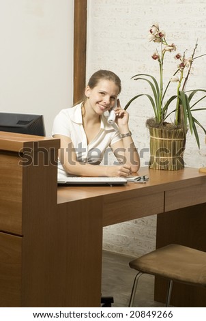 Smiling young secretary at a desk on the phone. Vertically framed photo.