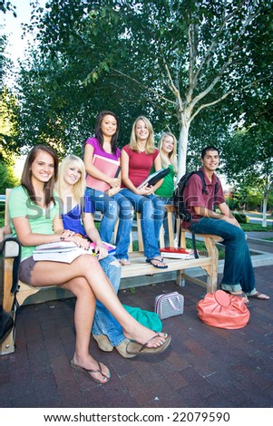 Group of five high school girls and one boy sitting on a bench holding books. Vertically framed photo.