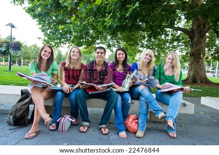 Smiling group of five high school girls and one boy sitting on a bench holding books. Horizontally framed photo.