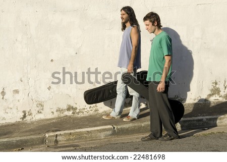 Two men walking down a street carrying guitars in guitar cases. Horizontally framed photo.