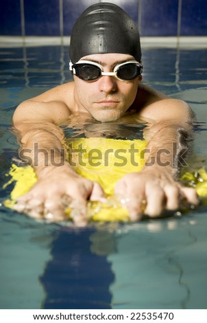Swimmer with a cap and goggles on swimming in a pool with a floatation device. Vertically framed photo.