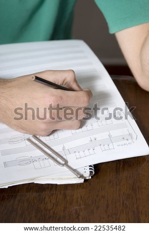 Man\'s hand writing music on a music sheet. Vertically framed photo.