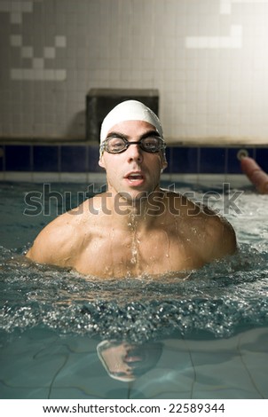 Man with a cap and goggles on swimming in a pool. Vertically framed photo.