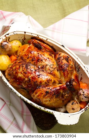 Baked whole chicken with garlic, potatoes and carrots in a vintage pot