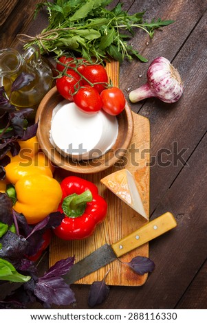 Bell peppers, basil, garlic, ricotta, goat cheese, tomatoes and arugula on a wooden table