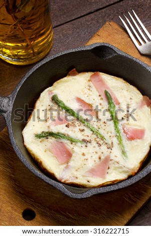 Omelet with asparagus and smoked pork in a cast iron skillet