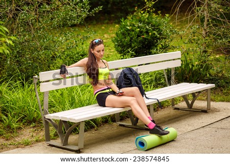 Young woman enjoying the music sitting on the bench in sport wear. Rest and relax after the training