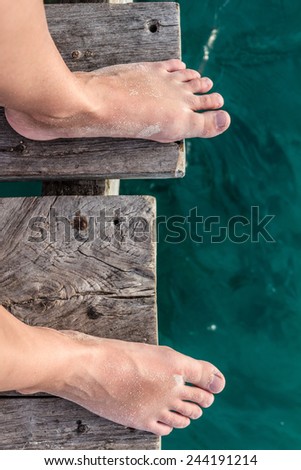 Bare feet standing by the ocean on a wooden pier POV shot