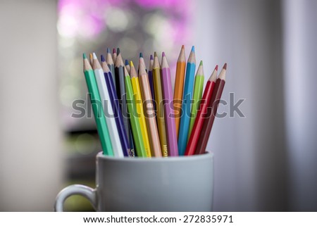 A group of color pencils in a white cup with a blurred garden background