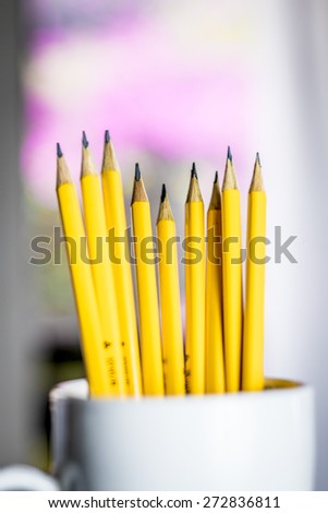 A group of yellow pencils in a white cup with a blurred background