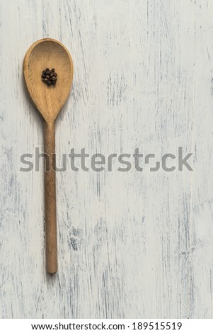 Wooden serving spoon with black peppercorns on white painted wooden surface