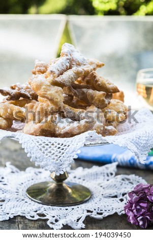 Frappe - typical Italian carnival fritters dusted with icing sugar, with a glass of desert wine in the background