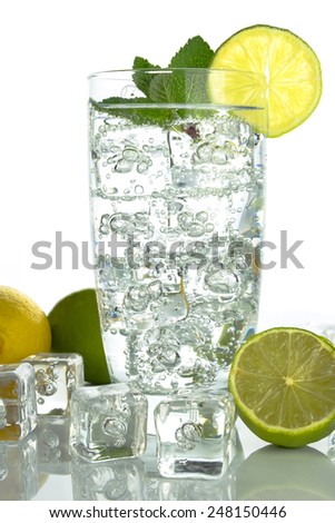 Glass of sparkling  water with ice cubes garnished with a slice of lime and mint on plain background