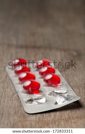 Red capsule medicine in blister package on wooden table. vertical photo, white background. Studio shot close up.