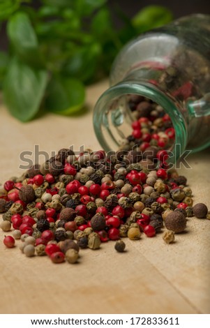 Heap of peppercorns on top of wooden table before glass jar and fresh basilica. Vertical photo. Selective focus on peppercorns. Recipe book photography.