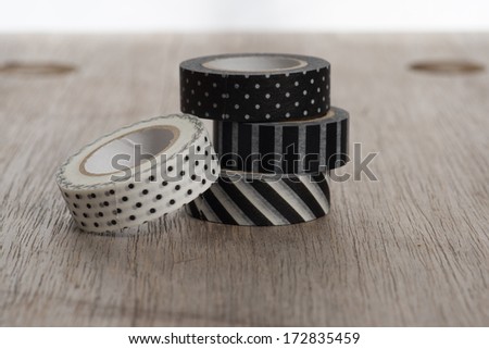 Washi tape rolls, masking tape rolls in pile on wooden bench. Black and white tapes.