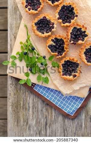 Eight small and fresh blueberry pies on wooden table from top. Bilberry pie on top of paper and linen. Fresh and tasty homemade blueberry pie.