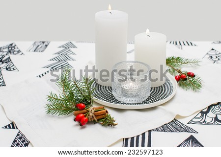 Christmas ornaments and candles on the table. white candles, glass object and ordnament on top of modern white linen tablecloth.