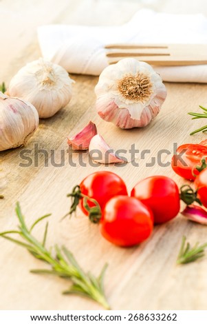 Fresh tomatoes, garlic and rosemary on wood table.   Cooking photo for recipe book or advertisement. healthy life.