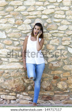 Portrait of beautiful dark-haired young woman wearing white t-shirt, surprised for the mobile