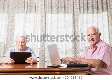 Happy smiling retired couple using computer laptop and tablet at home