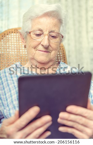 Portrait of a old woman smiling happily as she reads the screen on her tablet computer