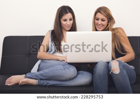 two women using laptop on sofa.