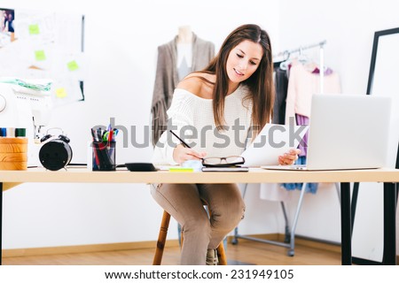 Young attractive female fashion designer leaning on office desk, working with a laptop at home