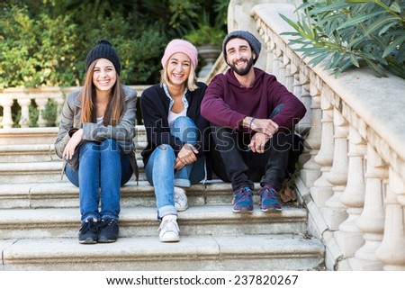 Group of friends two women and one man, sitting on a stairs in park
