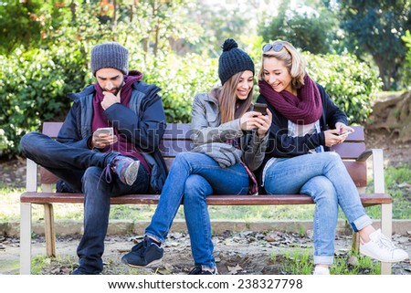Group of friends two women and one man, sitting on a bench in park