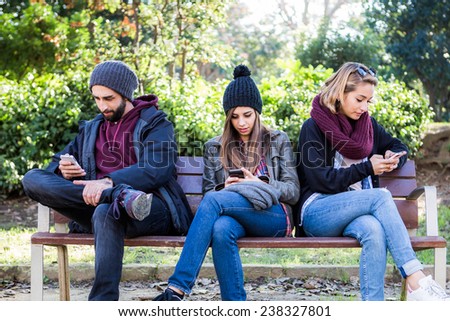 Group of friends two women and one man with mobile, sitting on a bench in park