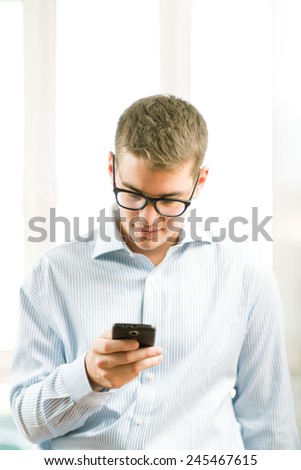 Handsome young businessman using mobile phone over blurred background in office