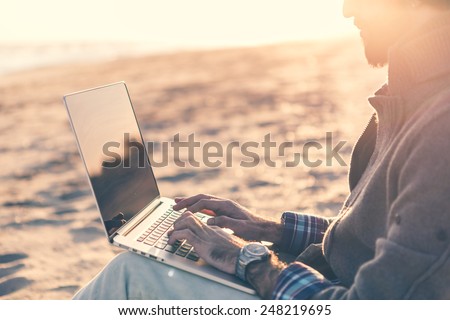 Man work on computer at the beach at sunset