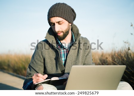 urban man sitting on a catwalk in the field enjoying nature working with a notebook and laptop