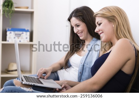two women using laptop and smiling on sofa in her home