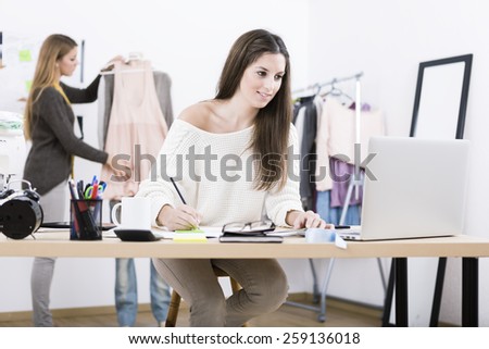 Young attractive females fashion designers leaning on office desk, working with a laptop