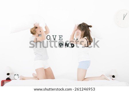happy laughing girls having a pillow fight on the bed at home