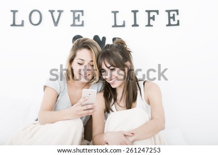 Two young roommates chatting with phone on the bedroom.