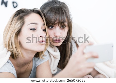 Two young roommates taking selfie with phone on the bedroom.