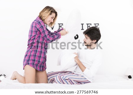 Young man and woman in bed. Couple pillow fight.