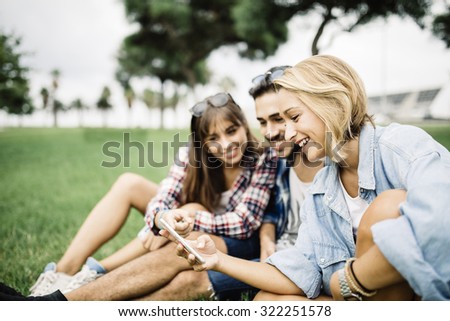 Group of friends two women and one man using a smartphone, sitting on floor in the park