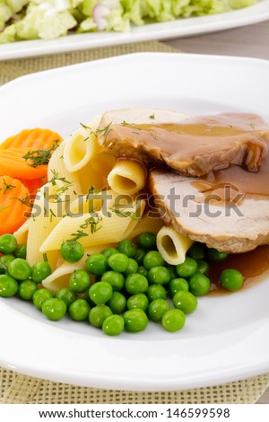 Roasted pork shoulder served with pasta and vegetables