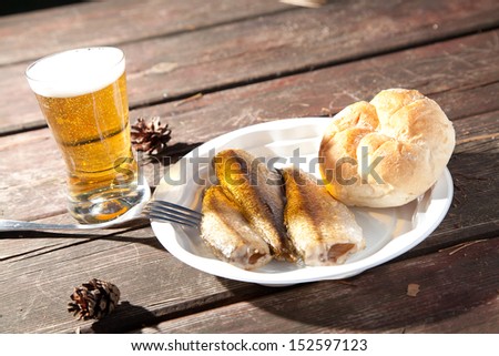 Fried fish on a plastic plate in the woods on a bench and drinking beer
