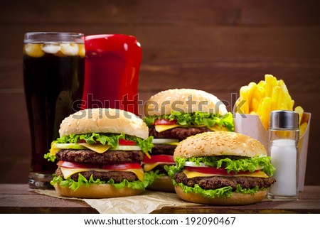Three hamburgers with fries, cola and ketchup on wood board