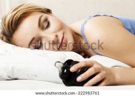 Beautiful young woman sleeping on bed with alarm clock in bedroom
