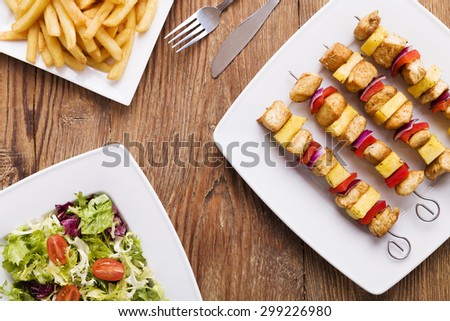Grilled chicken skewers with pineapple, peppers and onions served with french fries and vegetable salad