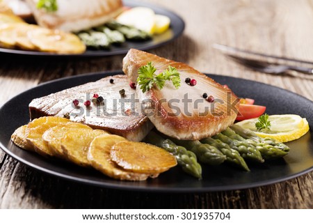 Grilled tuna steak served on asparagus with roasted zmieniakami on a black plate.